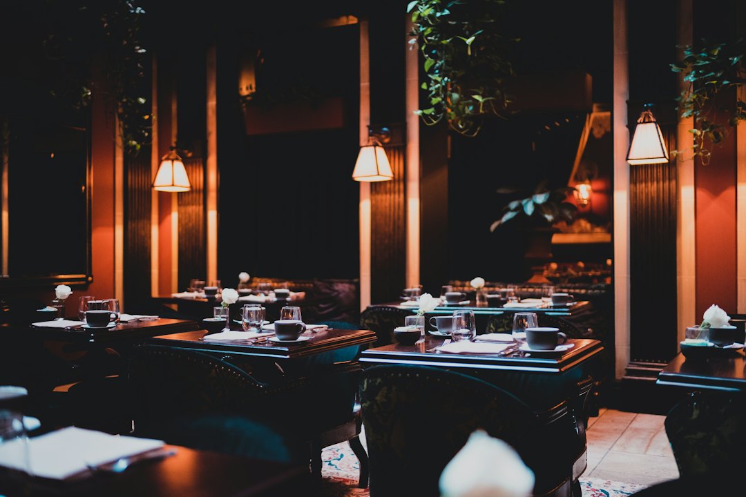 Salle de restaurant dans la pénombre, tables dressées sous des lampes suspendues
