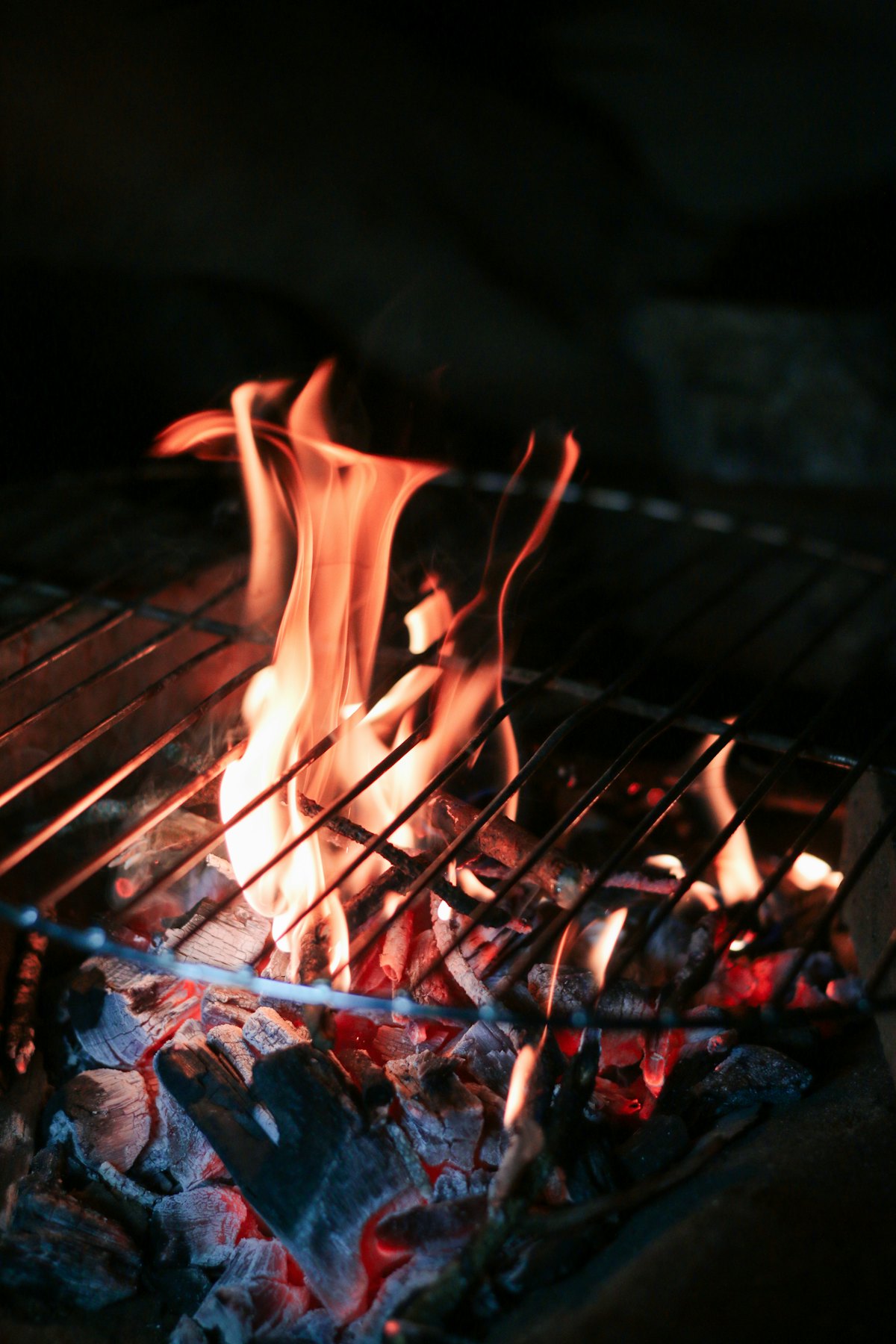Flammes vives au-dessus d’un lit de braises, sous une grille de cuisson