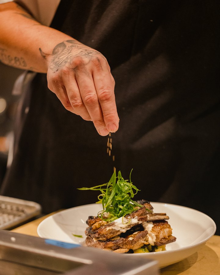 Mains d’un cuisinier qui parsème des herbes sur une assiette
