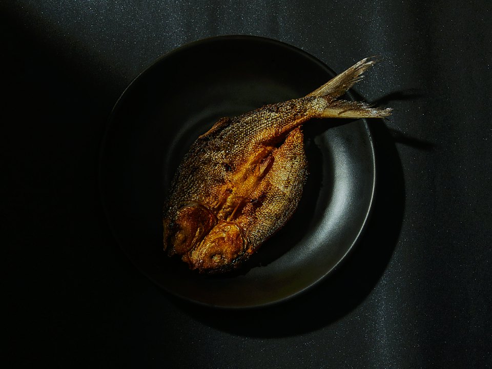 Poisson entier grillé, doré, dans une assiette noire