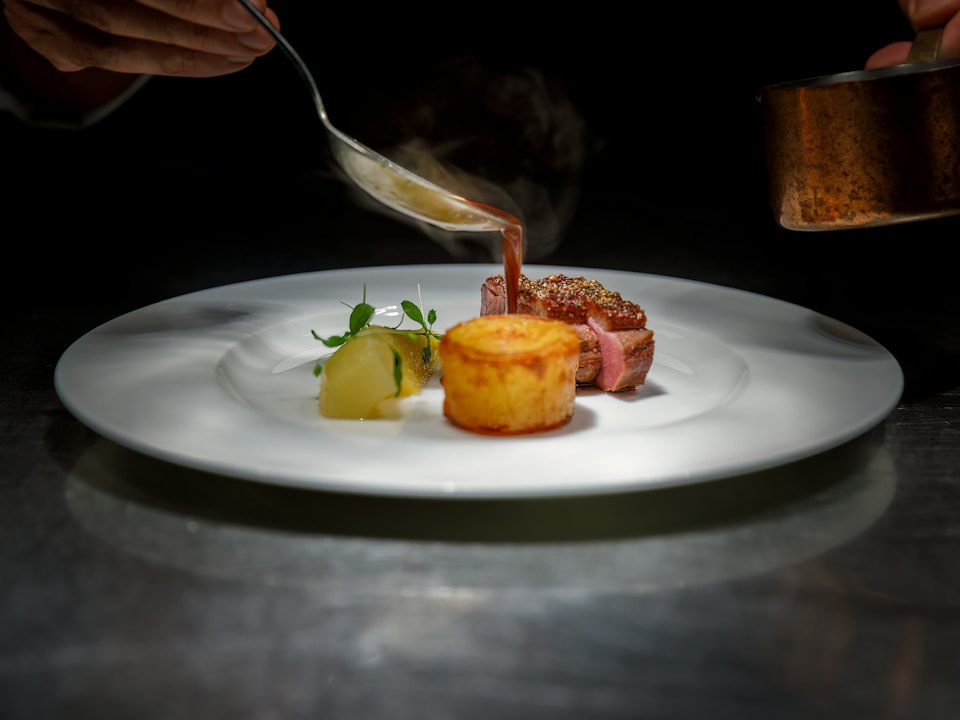 Sauce versée sur une assiette de canette et de pomme fondante